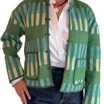 A person wearing a green patterned quilted jacket with vertical stripes in shades of green, beige, and light blue, styled over a white button-down shirt and dark blue jeans.