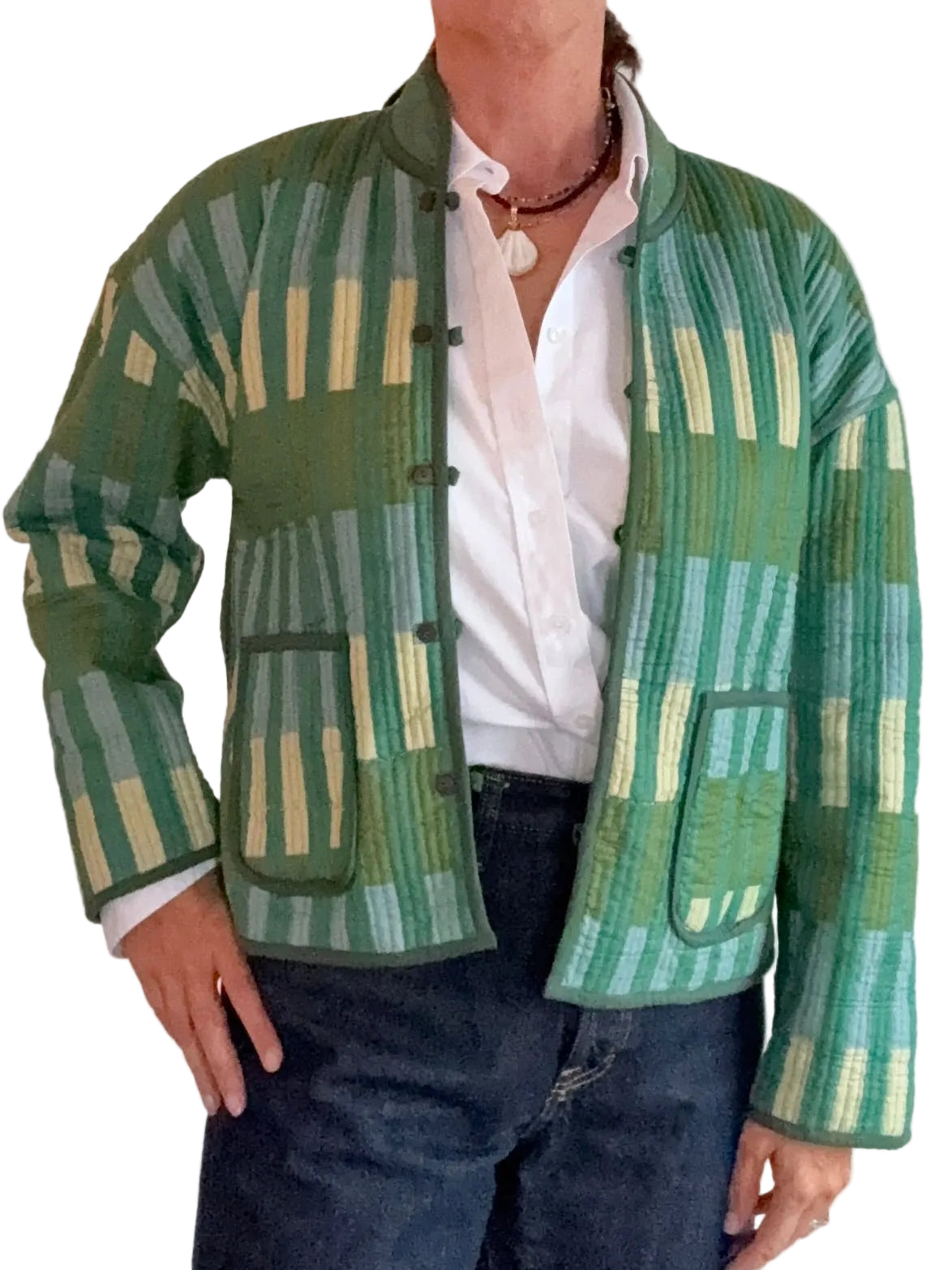 A person wearing a green patterned quilted jacket with vertical stripes in shades of green, beige, and light blue, styled over a white button-down shirt and dark blue jeans.