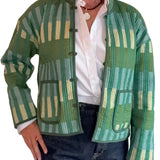 A person wearing a green patterned quilted jacket with vertical stripes in shades of green, beige, and light blue, styled over a white button-down shirt and dark blue jeans.